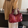 A deep red leather tote bag with a strap is displayed against a dark surface next to a beige coat.
