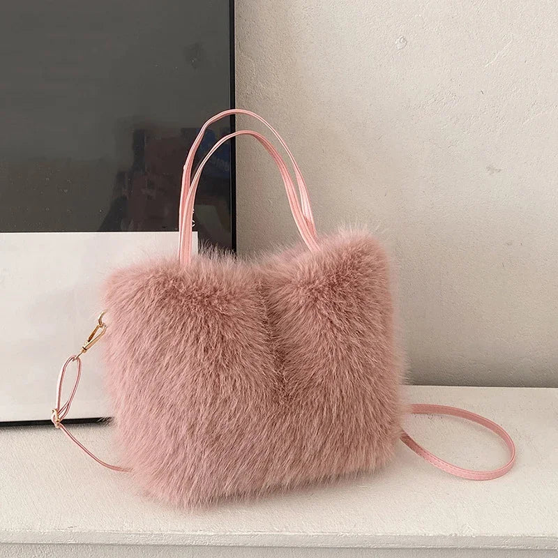 A soft pink plush faux fur tote bag with a thin pink strap resting on a white surface.