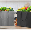 A set of three reusable black foldable grocery tote bags filled with fresh vegetables on a kitchen counter.