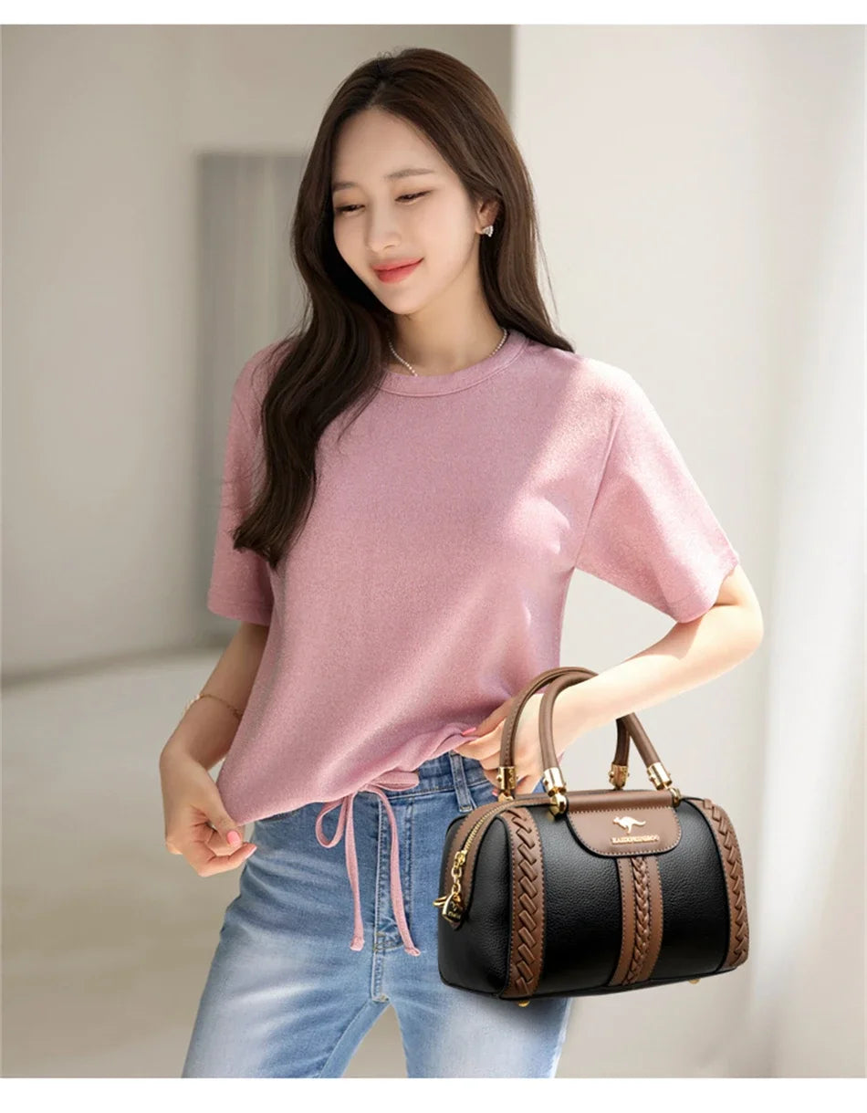 A young woman models a pink sweater and blue jeans while holding a brown and black leather shoulder crossbody bag.