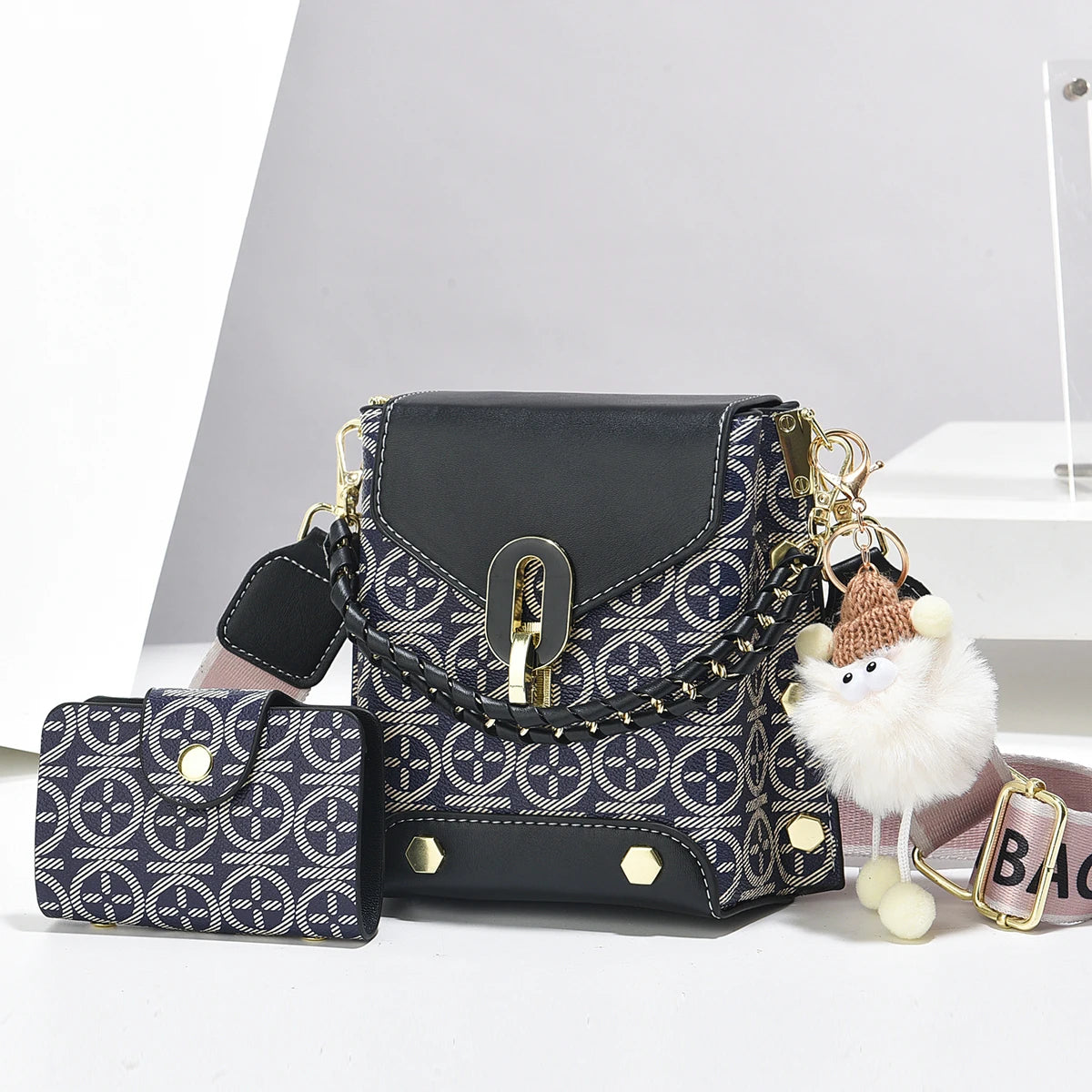 Un sac bandoulière en cuir faux noir avec des éléments dorés et un tissu à motifs, montré à côté d'une version plus petite.