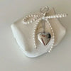 A silver heart pendant on a pearl string with a bow charm displayed on a white gift box.