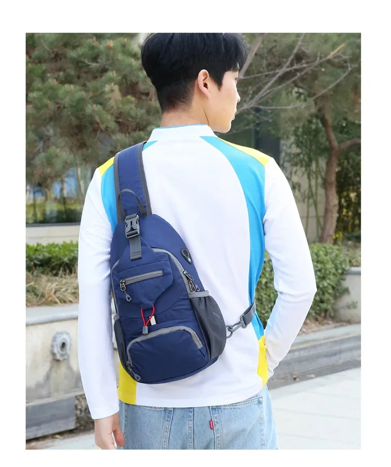 A person wearing a white long-sleeved shirt and jeans is holding a navy blue nylon chest sling bag.