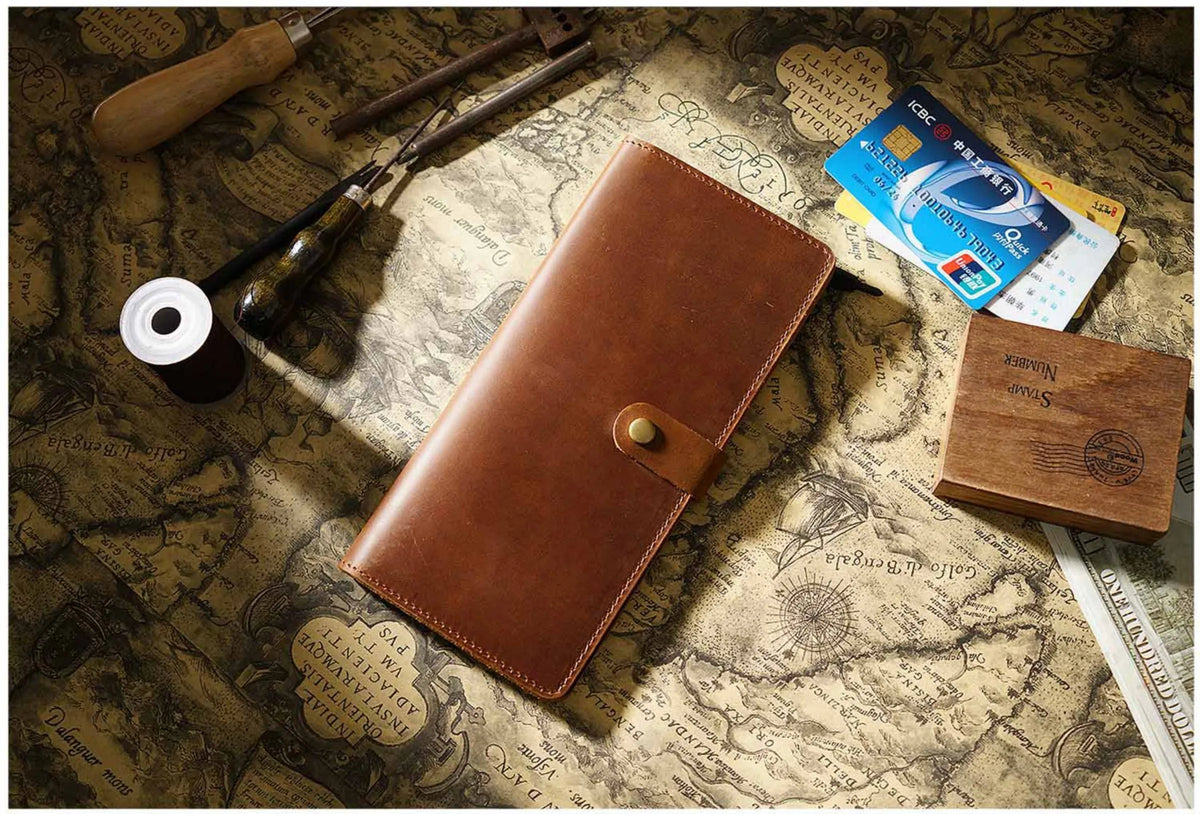 A brown genuine leather long bi-fold wallet with a snap closure resting on an old map background.