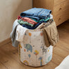 A woven laundry basket filled with folded denim and fabric, featuring elephant and animal illustrations.