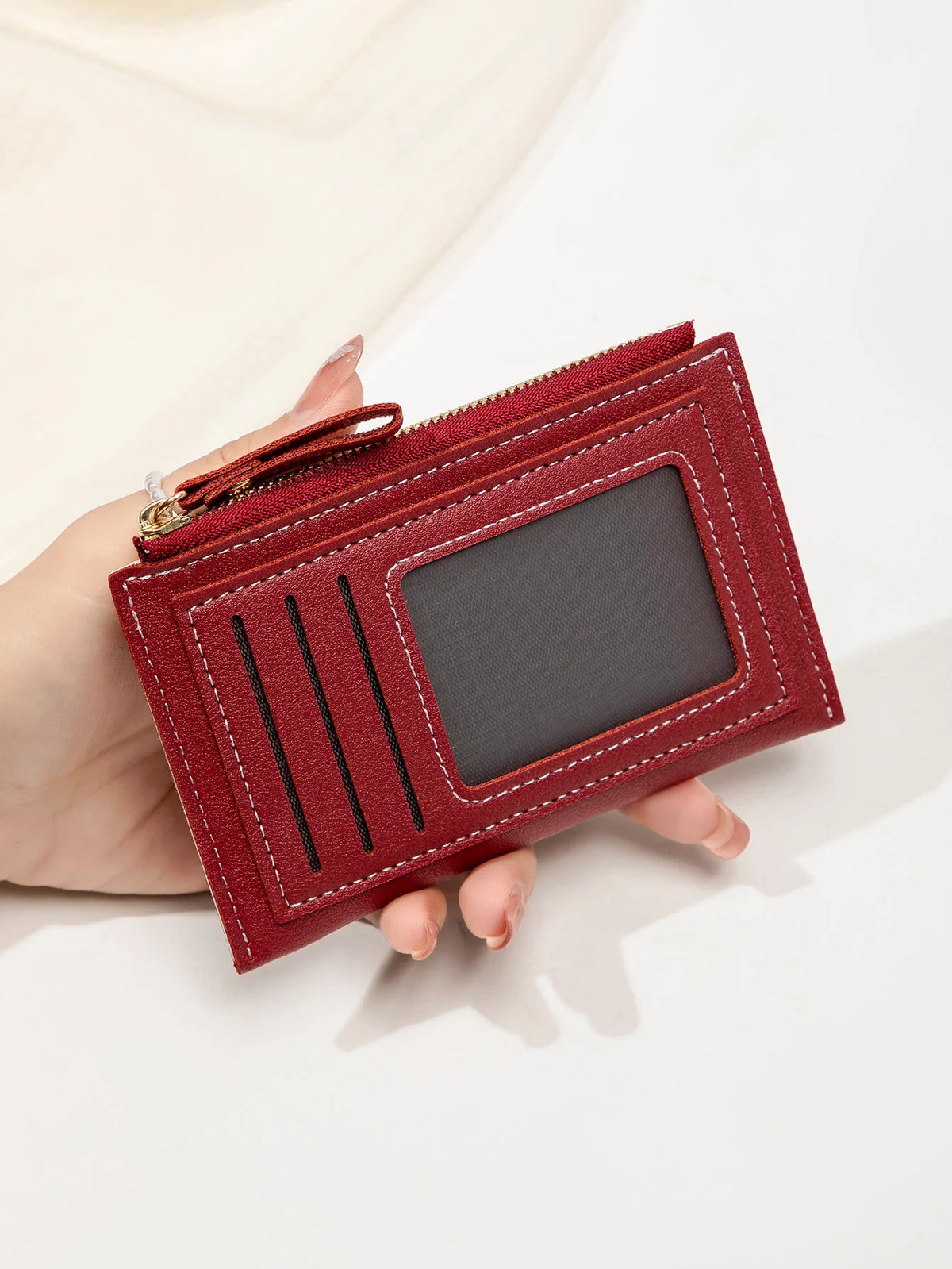 Gros plan d'un portefeuille en cuir PU marron avec fermeture éclair et fente rectangulaire, tenu dans une main.