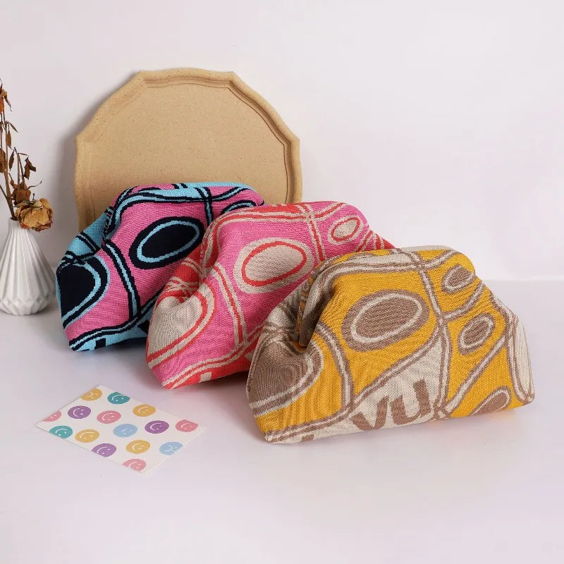 A collection of colorful knitted clip bags displayed in front of a beige backdrop.