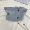 A light blue corduroy clutch bag with small brown bear embroidery, lying on a white surface.