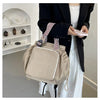 A beige nylon shoulder bag with a patterned strap is held by a person in a black blazer.