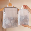 A white honeycomb mesh laundry bag is hanging from a wooden hook against a light wall.