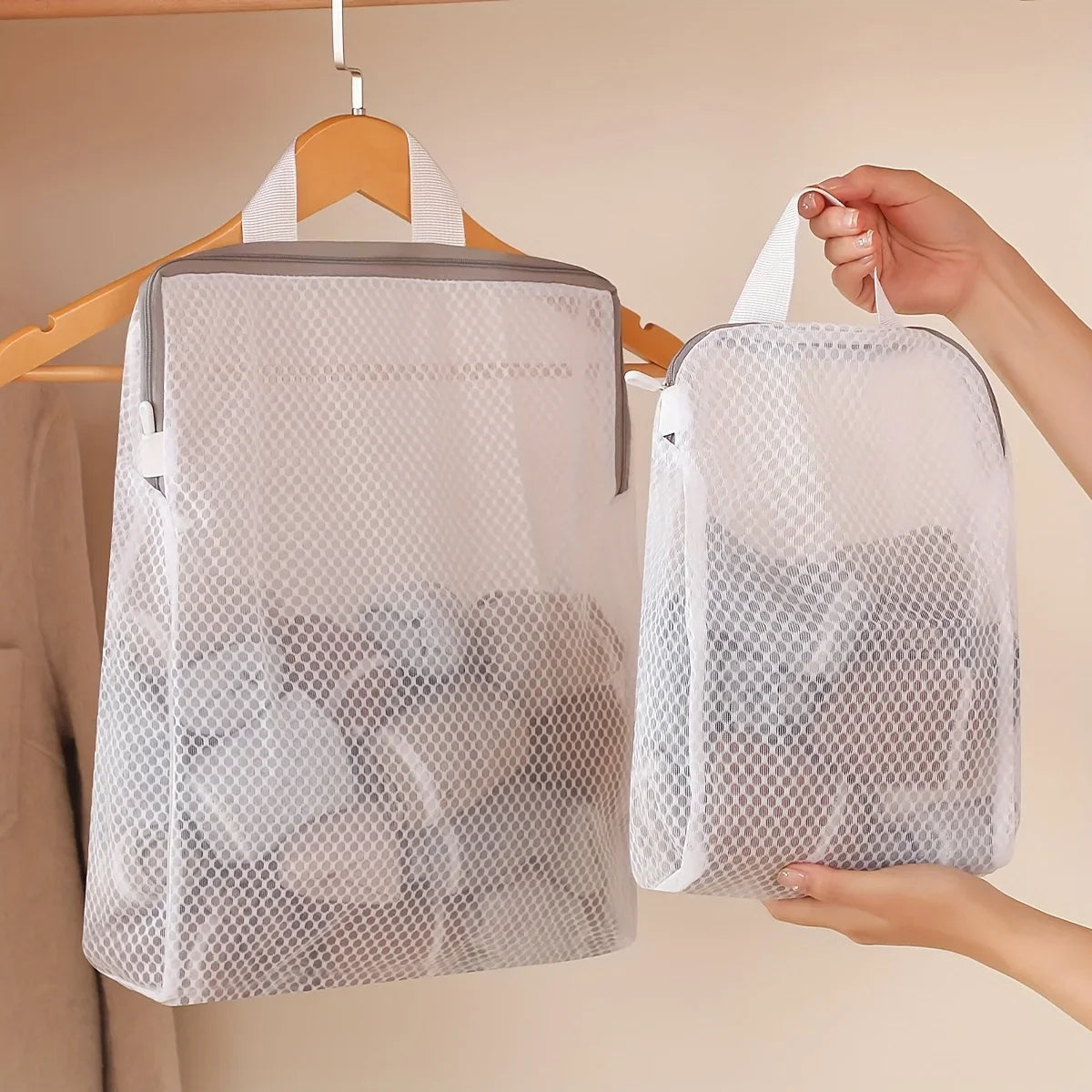 A white honeycomb mesh laundry bag is hanging from a wooden hook against a light wall.