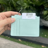 A hand holds a light mint green genuine leather zipper card holder with a silver clasp and a white tag.