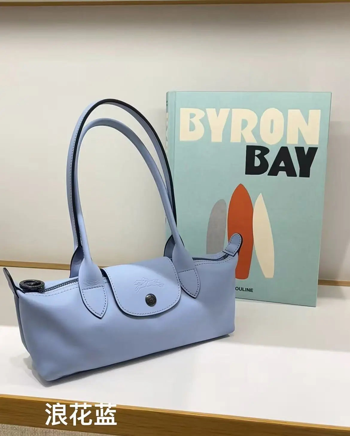 A light blue storage shoulder bag is displayed next to a book titled Byron Bay.