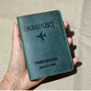A dark green genuine leather passport holder with a silver airplane emblem is held in a hand.