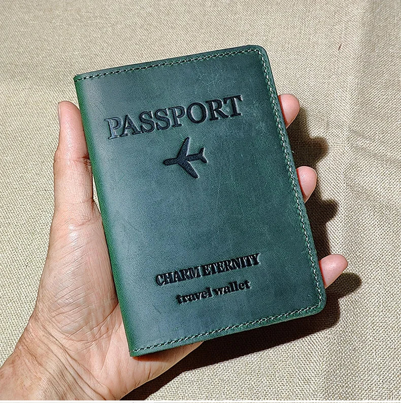 A dark green genuine leather passport holder with a silver airplane emblem is held in a hand.