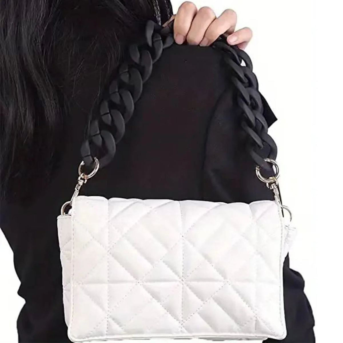 White quilted leather handbag with a black chunky chain shoulder strap being held by a person.