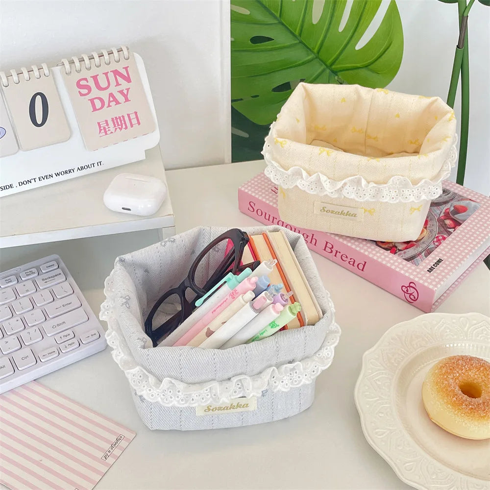 A light pink fabric storage basket with a heart and bow is shown next to stationery and a green plant.