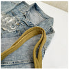 A denim jacket with a mustard yellow corduroy strap and clear acrylic embellishments.