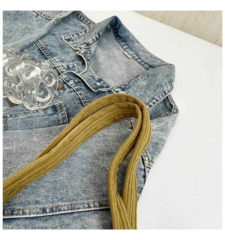 A denim jacket with a mustard yellow corduroy strap and clear acrylic embellishments.