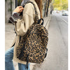 A woman wearing a beige coat and jeans carries a leopard print canvas backpack while walking on a city sidewalk.