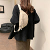 A woman is holding a beige corduroy crossbody waist bag with an adjustable strap against a white wall.