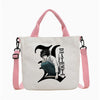Bolso tipo tote blanco con gráfico negro de un personaje y el texto DEATHNOTE, sujetado por correas rosas.