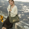 A young woman wearing a light yellow patterned sweater and a brown skirt is posing outdoors with a large olive green cotton c