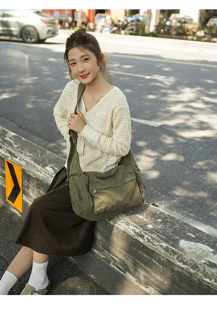 A young woman wearing a light yellow patterned sweater and a brown skirt is posing outdoors with a large olive green cotton c