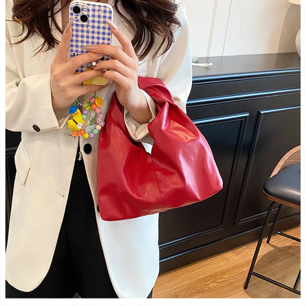 A woman holds a red leather crossbody tote bag against a white blazer.