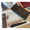A dark brown patterned zippered wallet with a gold accent is shown resting on a wooden table next to several beige cards.