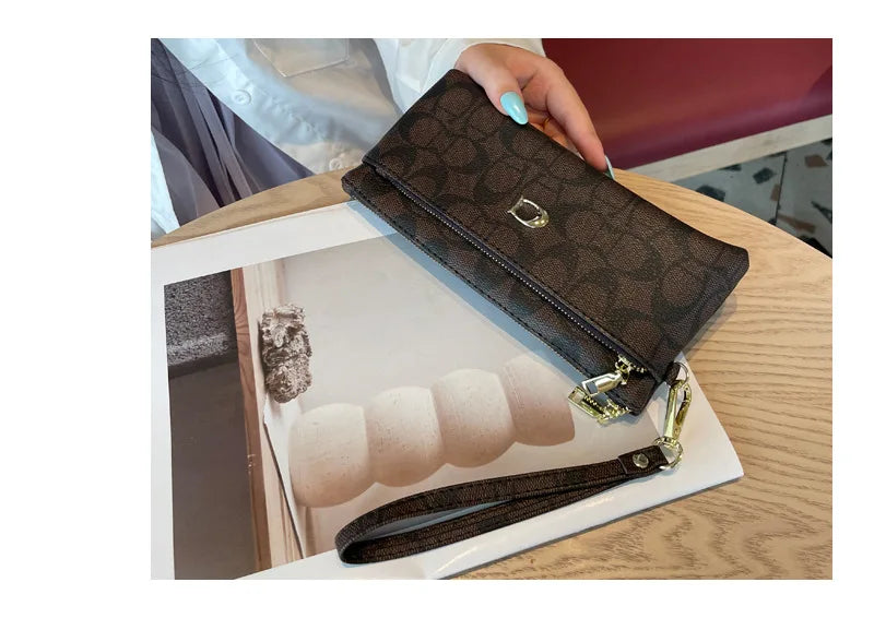 A dark brown patterned zippered wallet with a gold accent is shown resting on a wooden table next to several beige cards.