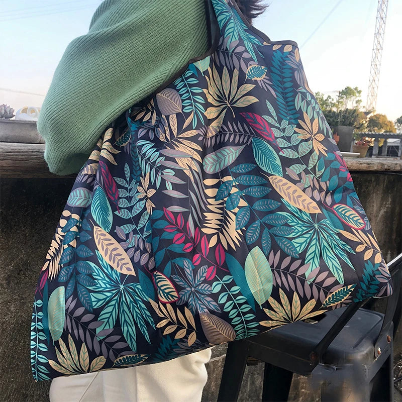 A close-up of a patterned fabric shopping tote with a green sleeve and strap, resting on a dark surface.