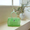 Limettengrünes Sommer-Gelidertasche mit weißem Riemchen und einer blättrigen Pflanze in einer weißen Vase auf einem Fensterbr