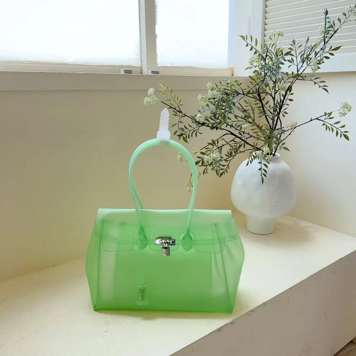 Limettengrünes Sommer-Gelidertasche mit weißem Riemchen und einer blättrigen Pflanze in einer weißen Vase auf einem Fensterbr