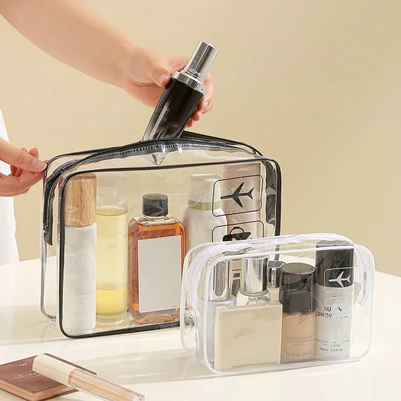 A hand is opening a clear PVC toiletry bag with a zipper closure, revealing various skincare products inside.