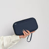 A hand holds a dark navy blue multi-functional passport and document organizer against a light background.