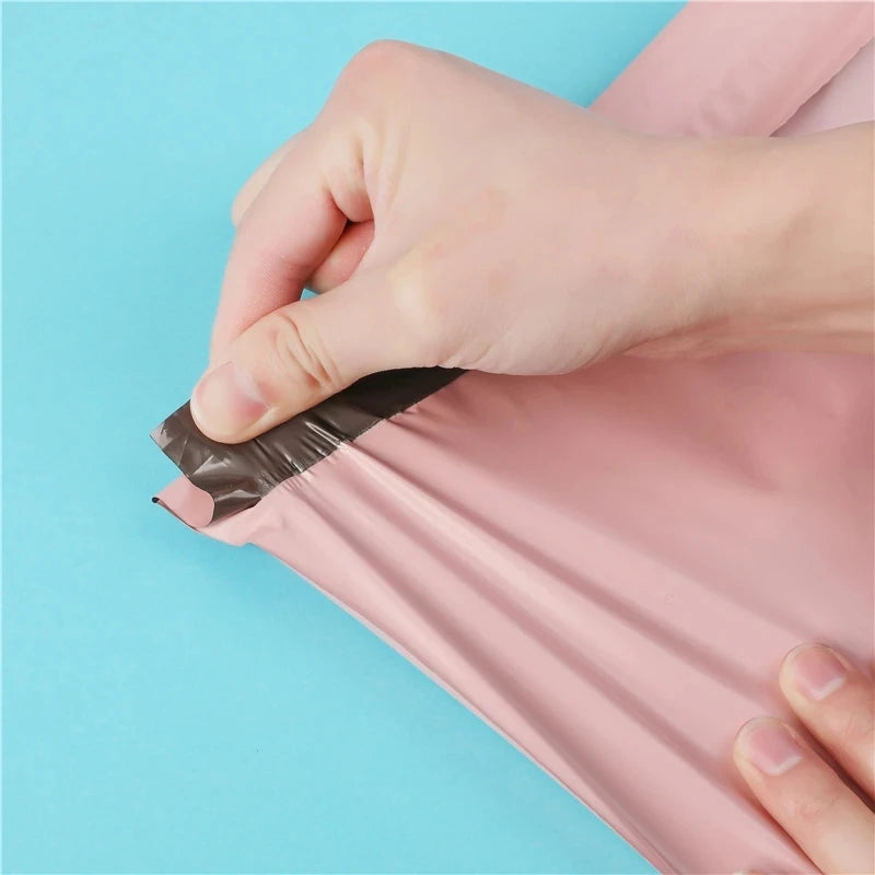Una mano sella una bolsa de almacenamiento rosa autoadhesiva para envío o embalaje.