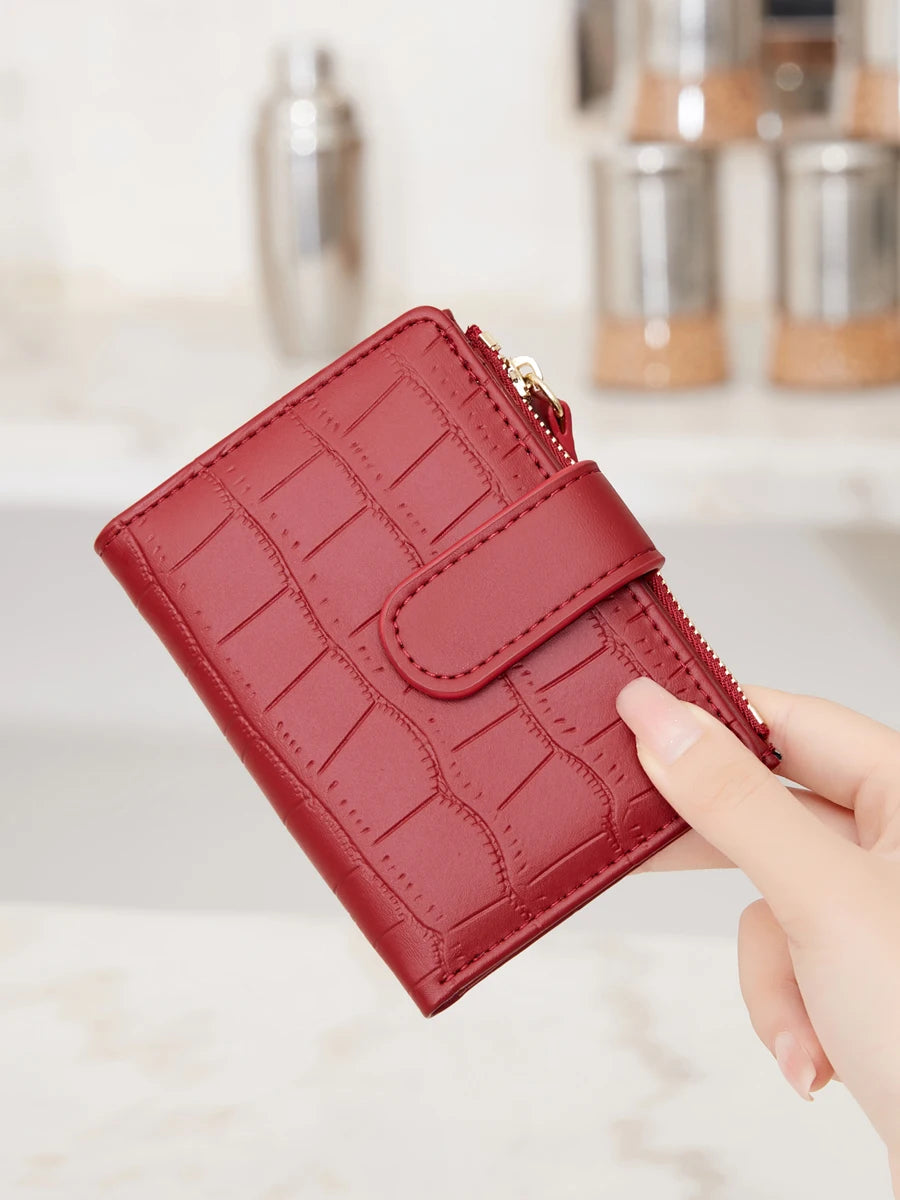 A close-up of a red quilted PU leather bifold wallet with a zipper, held by a hand.