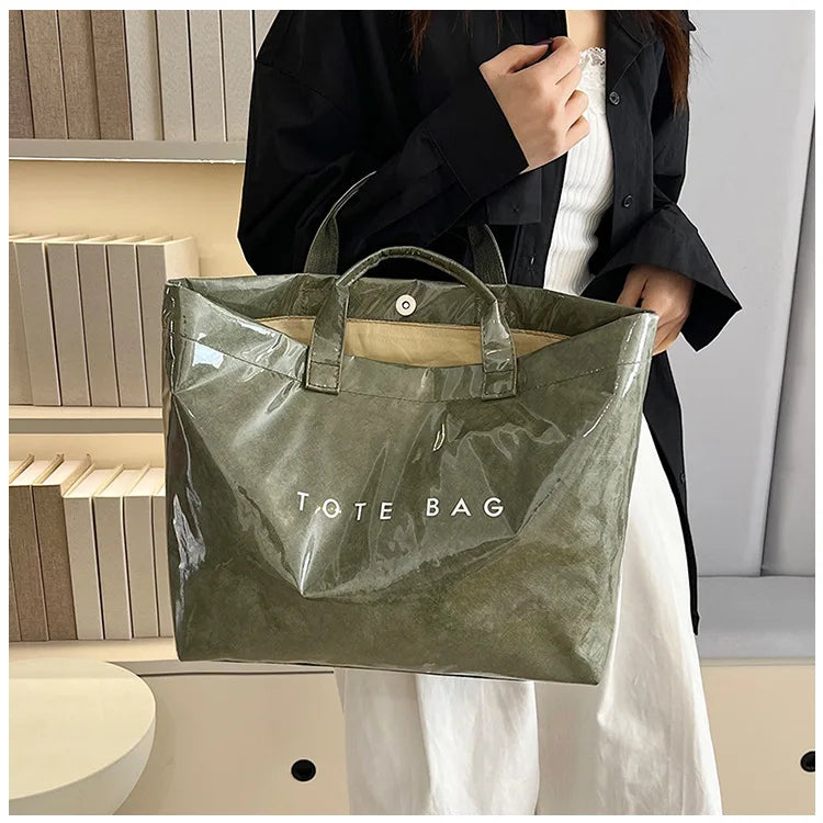 A woman holds a olive green transparent waterproof PVC tote bag against a light background.