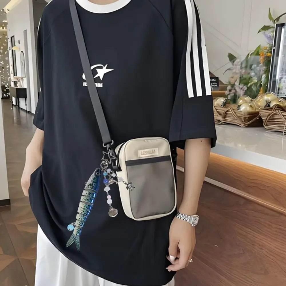 A person is holding a black t-shirt featuring a silver fish keychain and a light gray pouch keychain.