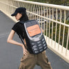 A woman wearing a black shirt and tan pants carries a black vintage Y2K telephone backpack outdoors.