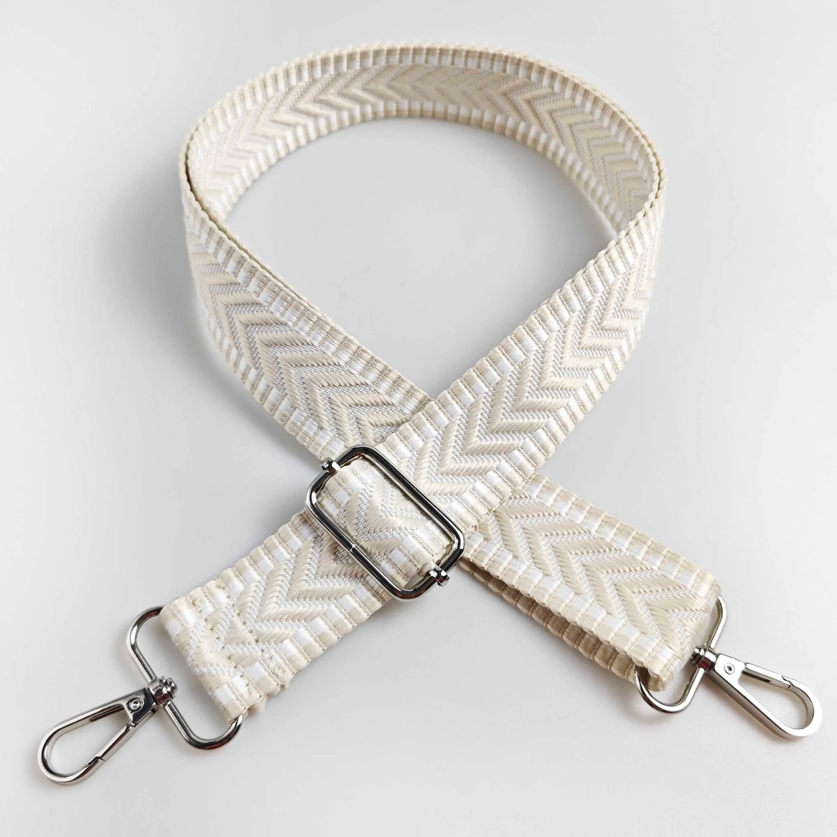 A beige woven strap with an arrow jacquard pattern, featuring metal hardware for a handbag.