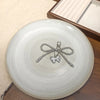 A silver pearl keychain with a bow knot is displayed on a round, speckled white ceramic plate.