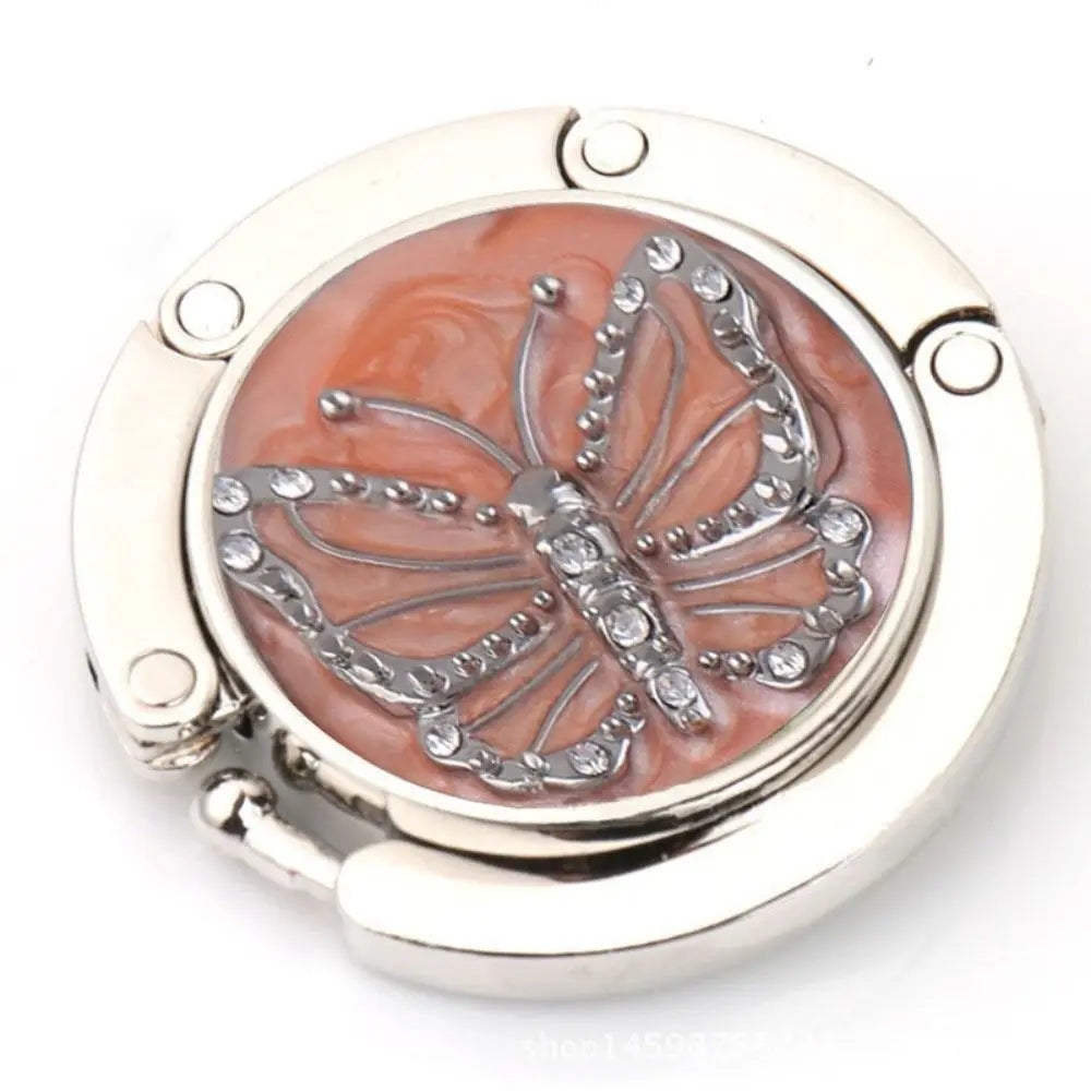 Gancho de soporte plegable de aluminio plateado con diseño de mariposa color oro rosa.