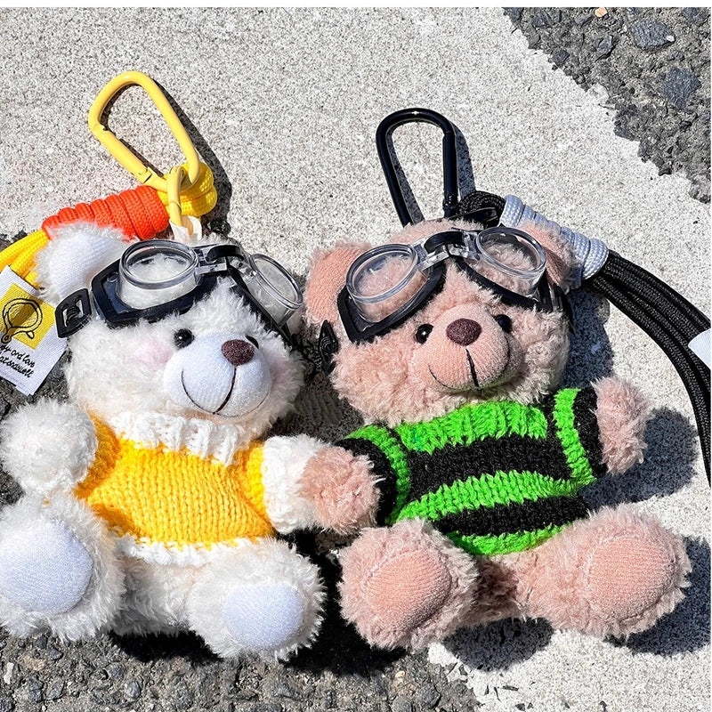 A fluffy pink bear plush toy with black glasses and a camera attached to a keychain.