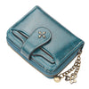 A teal leather mini wallet with stitching and a gold charm is shown at an angle.