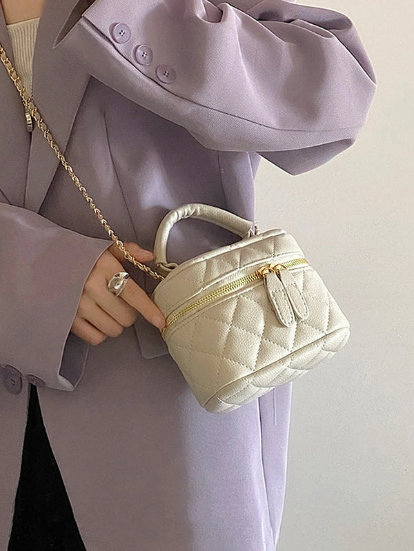 Une main tient un petit sac bandoulière matelassé beige clair avec une chaîne dorée, contre un blazer lavande.