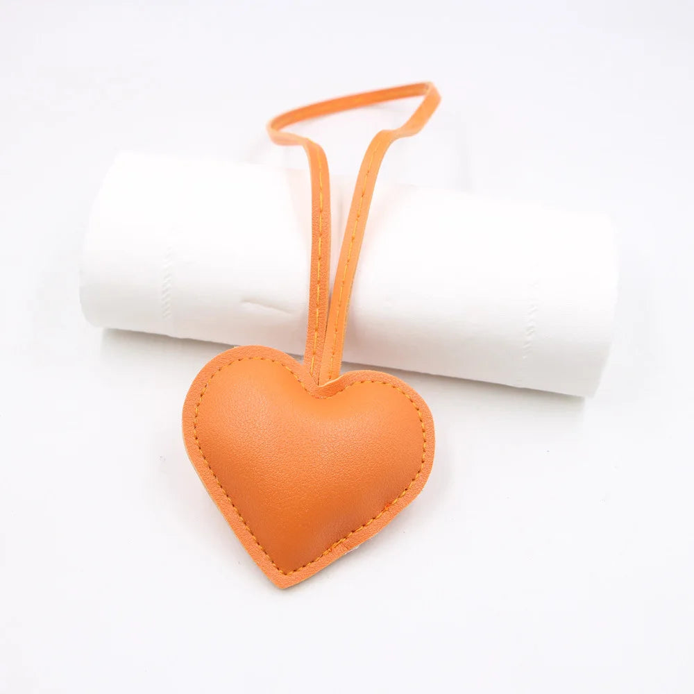 An orange PU leather heart shaped keychain attached to a white cylindrical object.