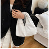 A woman holds a white minimalist crossbody tote bag against a black blazer and a white skirt.