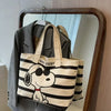 A beige and black striped canvas shoulder bag featuring a Snoopy cartoon face design, displayed on a hanger.
